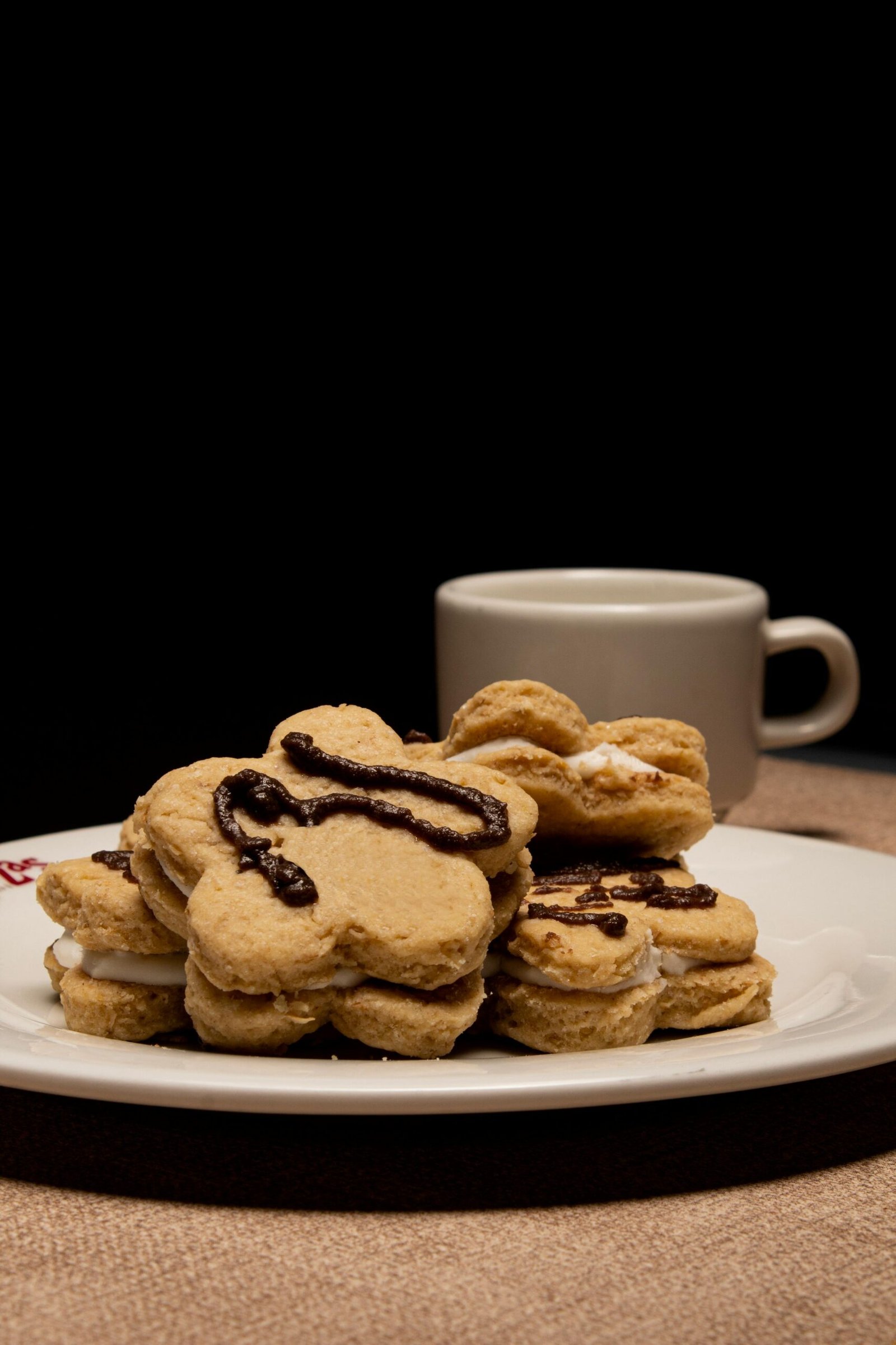 Mouth-watering flower-shaped cookies adorned with chocolate drizzle on a plate with coffee.